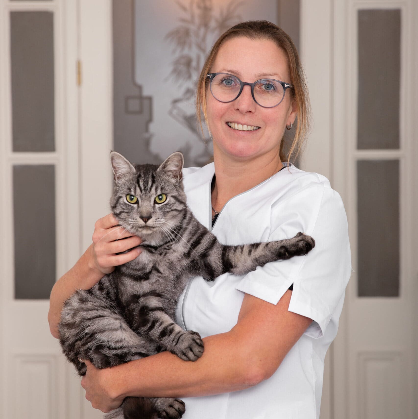 Medewerker in witte dienstkleding met een grijs gestreepte kat op de arm.